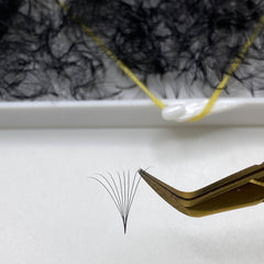 Eyelash extensions black clustered lashes with gold tweezers on white surface