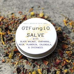 Salve with GTFungiO label, round silver tin, surrounded by colorful dried herbs and flowers