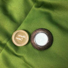 Round compact mirror with brown ribbed frame and clear lid, on green fabric