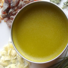 Yellow salve in metal tin with brown and white ingredients around it