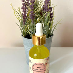 Makeup remover bottle with yellow liquid, gold cap, and white dropper, in front of purple flowers