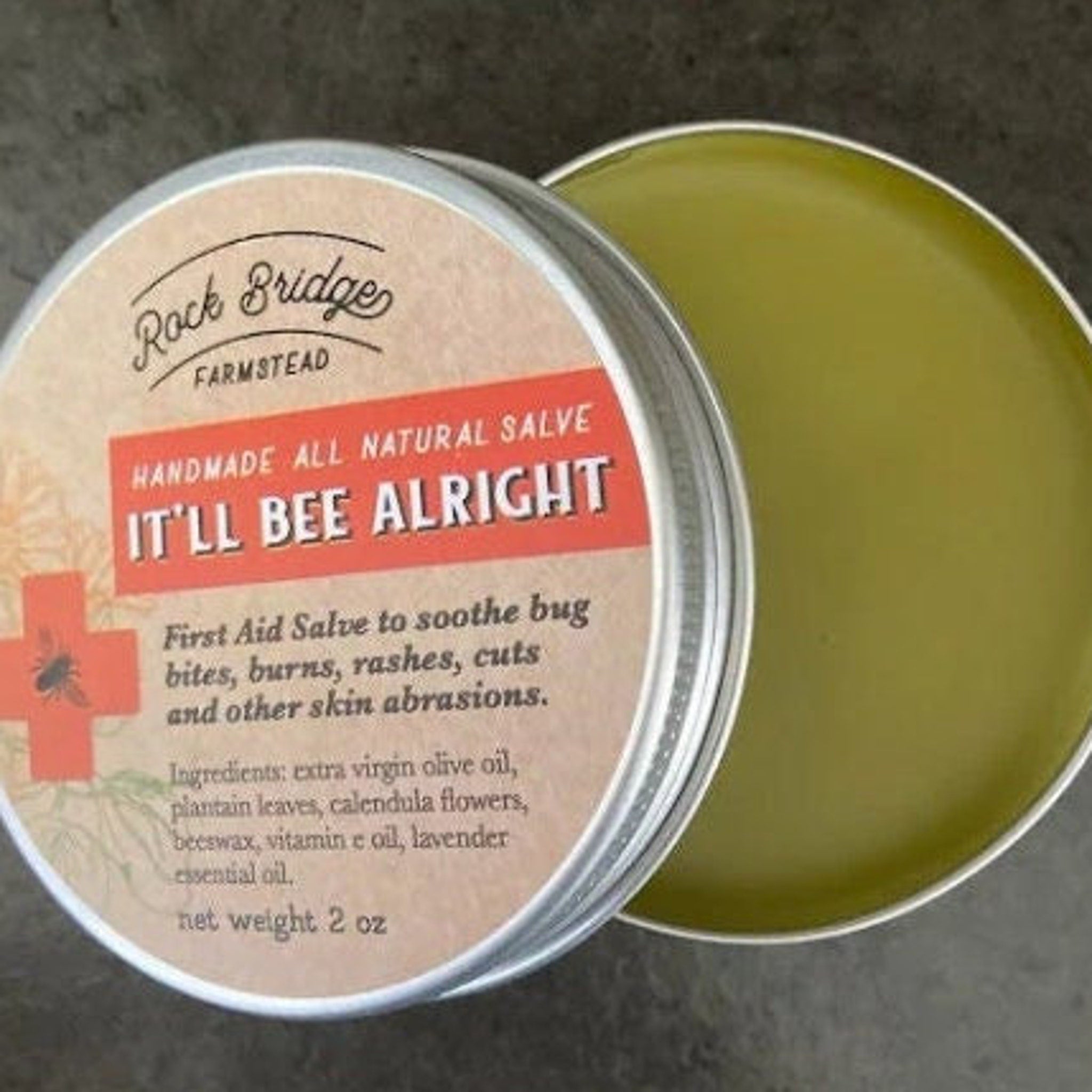 Lip balm jar with green salve, silver metal rim, and "It'll Bee Alright" label