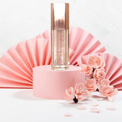 Lip gloss bottle with metallic cap, clear glass, and pink background with flowers