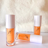 Lip oil bottles with orange liquid, white caps, and JC logo