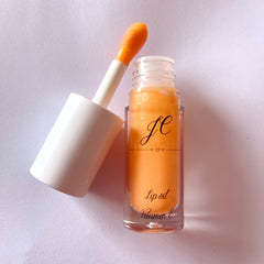 Lip oil with orange liquid, white applicator, and clear glass bottle with text