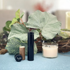 Lip balm tube black and brown with "hylo" text and a candle in a glass jar on blue fabric