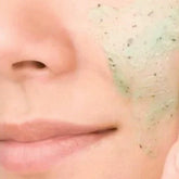 Facial Cleanser with green and black scrub applied to face, close-up view