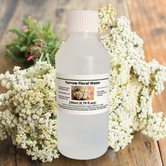 Close-up of yarrow floral water misting from an elegant glass bottle with gold accents, showcasing its fine spray and delicate texture