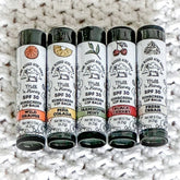 Lip balm tubes with black caps, white labels, and colorful flavor bands, One Blessed Acre Farm brand