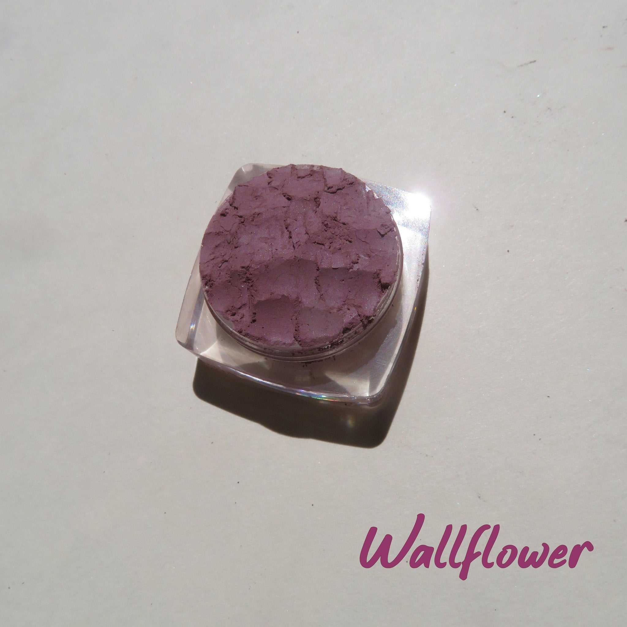 Close-up of matte purple mineral eyeshadow in a small round jar with black lid, showcasing loose pigment texture.