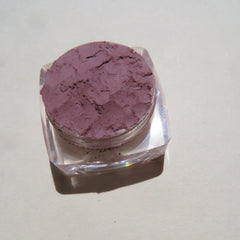 Hand applying matte purple mineral eyeshadow with a brush, showcasing loose pigment texture and vegan formula.