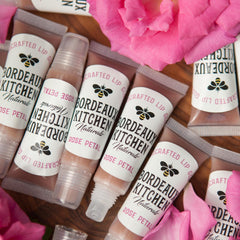 Lip gloss tubes with clear and white label, Bordeaux Kitchen Naturals brand, rose petals visible