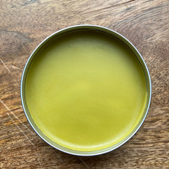 Yellow balm in a silver tin on a wooden surface, top-down view
