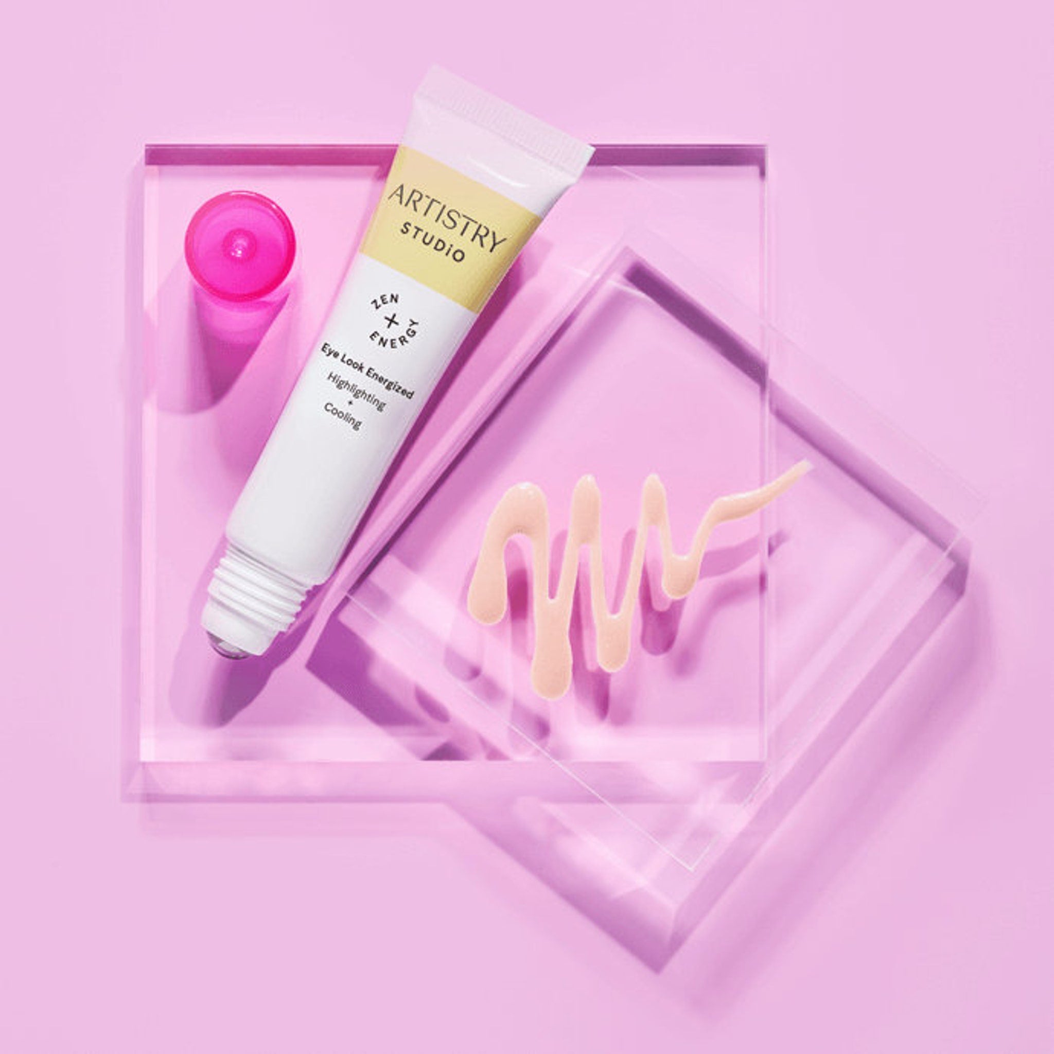 Eye makeup serum tube, white and yellow tube, pink serum on clear acrylic platform, Artistry Studio visible