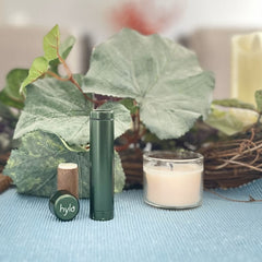 Hylo lip balm in green tube with brand, and candle on blue textured surface