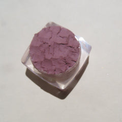 Purple powder eyeshadow in clear plastic container with textured surface and square shape