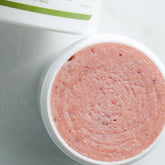 Sugar scrub in white container with pink scrub and dark flecks, top view