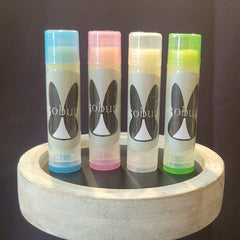Lip balms, four tubes with colorful caps, CocoBunny logo, on a white wooden tray