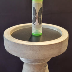 Lip balm tube with "cobun" text, green and clear, on a white wooden stand with black surface