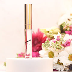 Lip gloss tube with clear gloss, gold cap, and A.Monét branding on white stand