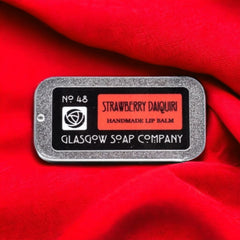 Lip balm tin with silver frame, red label, and Glasgow Soap Company text on red fabric