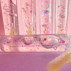 Lipgloss with pink glitter, clear tube, and "Heart Strings" text on pink background