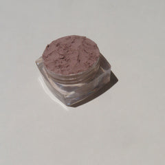Hand applying matte brown mineral eyeshadow with brush, showcasing loose pigment texture and natural finish.