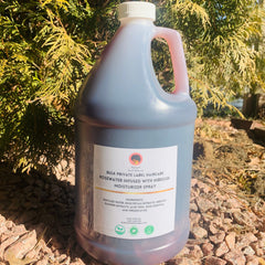 Side view of rosewater gallon with matte white label and silver spout against neutral backdrop