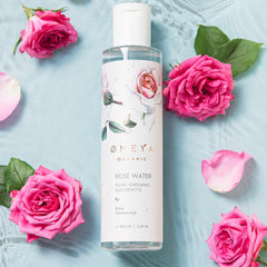 Rose water bottle with pink roses, green leaves, and O MEYA branding on a blue surface