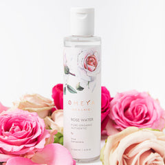 Rose water bottle with white label, floral design, surrounded by pink roses, OMEYA brand visible