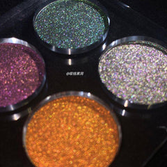 Eyeshadow pans with shimmering multi-color glitter, round metal containers, four shades visible