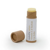 Lip balm tube with brown cardboard, white label, and yellow balm visible, Rooted by Nature brand