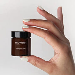 Eye cream jar, brown glass, black lid, held in hand, "mokann" brand visible