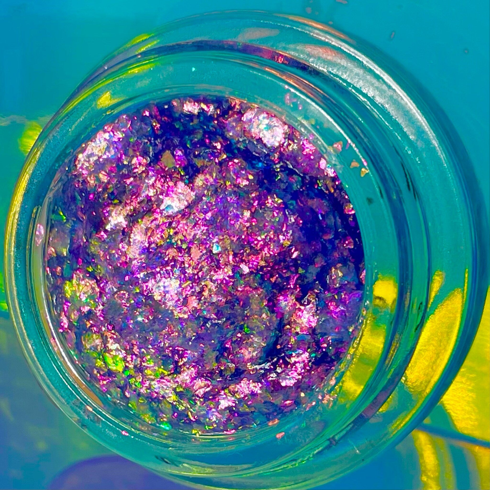 Shimmery holographic eye shadow pot with iridescent flakes in shifting rainbow hues, clear gel base