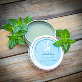 Mint leaf salve in silver tin with green leaves on wood surface, Dry Hollow Farm text visible
