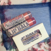 Lip balm tubes with pink and purple labels, white box, on blue mesh fabric