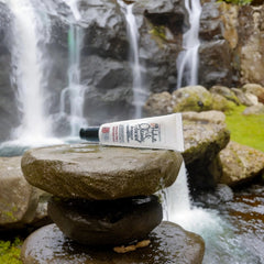 Facial cleanser tube, white with black cap, EvenMelanin brand on rocks near waterfall