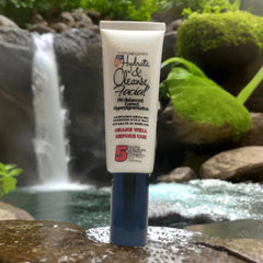 Facial cleanser tube, white and blue container, Even Melanin brand name visible, in natural setting