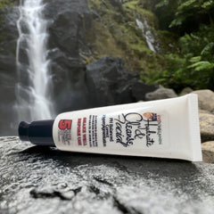 Facial cleanser tube with white, blue, and black colors, text of Even Melanin Hydrate & Cleanse Facial, on a rock