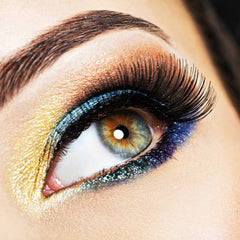 Eye makeup with gold, blue, and black glitter applied, close-up of eye with long lashes