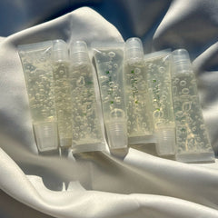 Lip gloss tubes, clear with bubbles, white plastic, "Aloe Vera" text on tubes, on white fabric