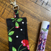 Lip balm holder with black cherry print fabric and metal clip, next to lip balm tube