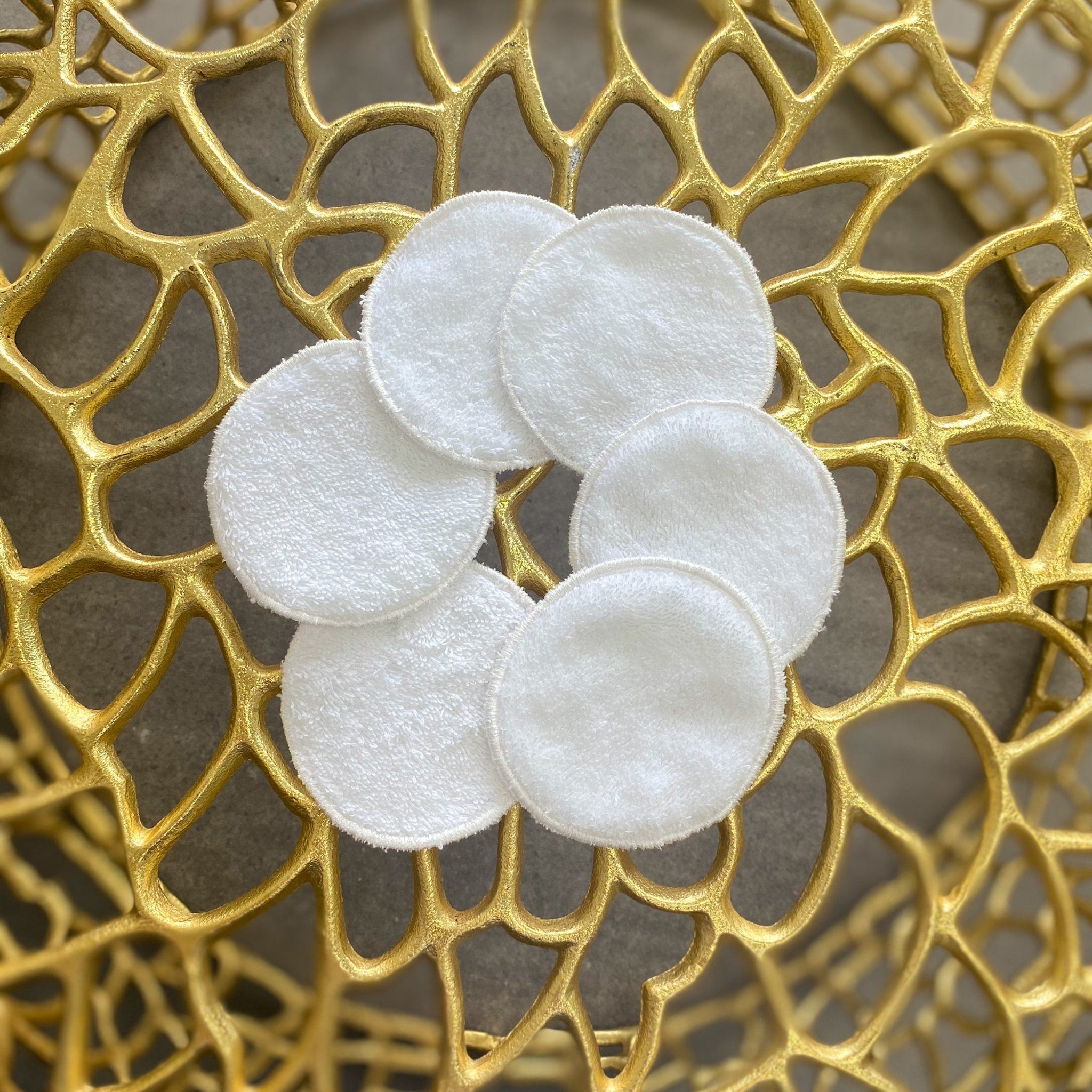Makeup remover pads, white cotton rounds, arranged in a flower shape on gold surface