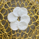 Makeup remover pads, white cotton rounds, arranged in a flower shape on gold surface