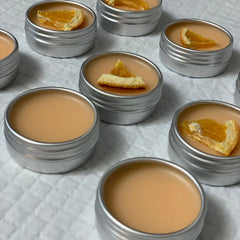 Lip balm in silver tins, peach color, with orange slice garnish