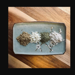 Clay powders in brown, white, and green on a light blue ceramic tray with floral design, on a wooden surface