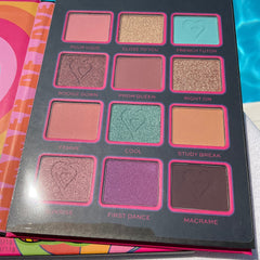 Eyeshadow palette with various colors, heart imprint, and pink trim on a dark gray background