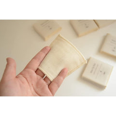 Reusable cotton pad, cream fabric, square shape, held in hand with other pads in background