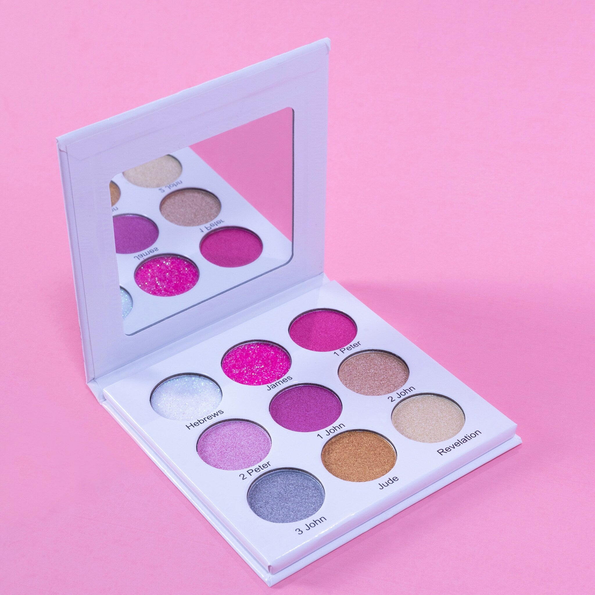 Eyeshadow palette with multiple colorful shades in white compact, open with mirror on pink background