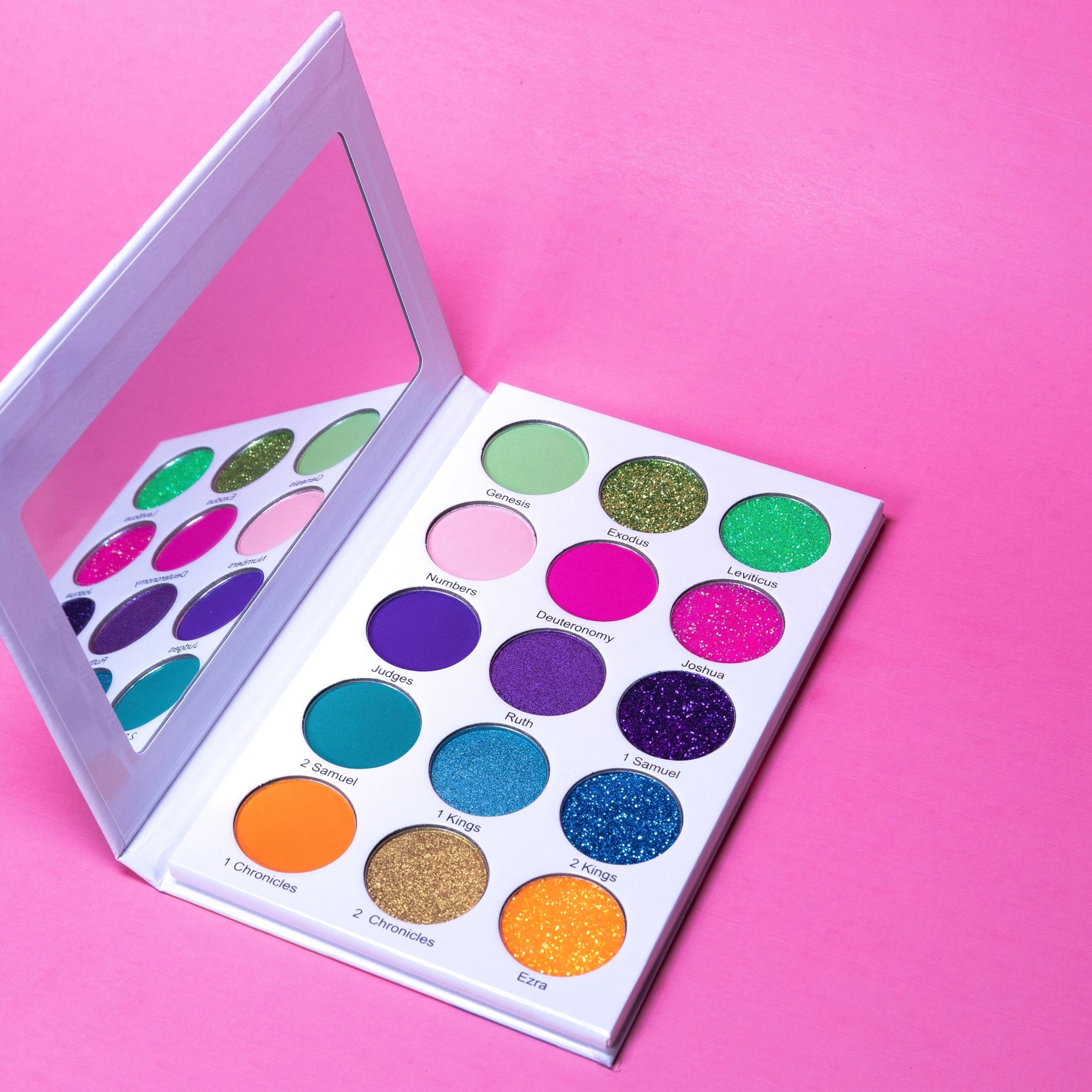 Eye makeup palette with colorful eyeshadows, white case, and mirror on pink surface